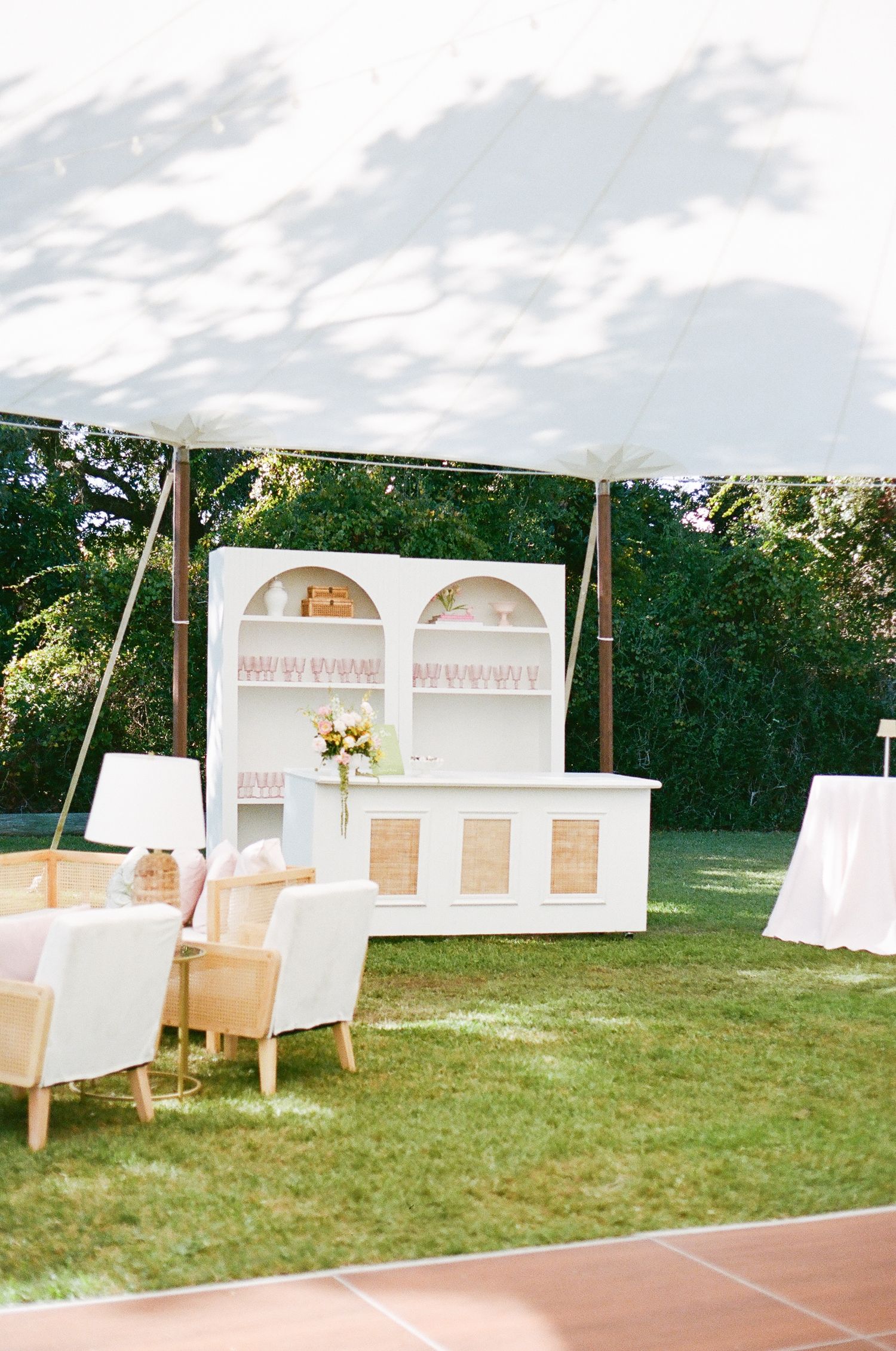 Elegant white display cabinet with floral arrangements set up outdoors on grass for an event under a tent canopy.