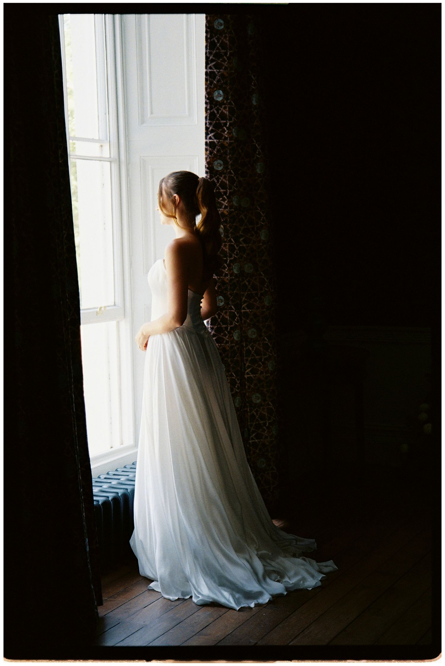 A quiet moment of the bride looking out of the window on 35mm film. Bridal silhouette.