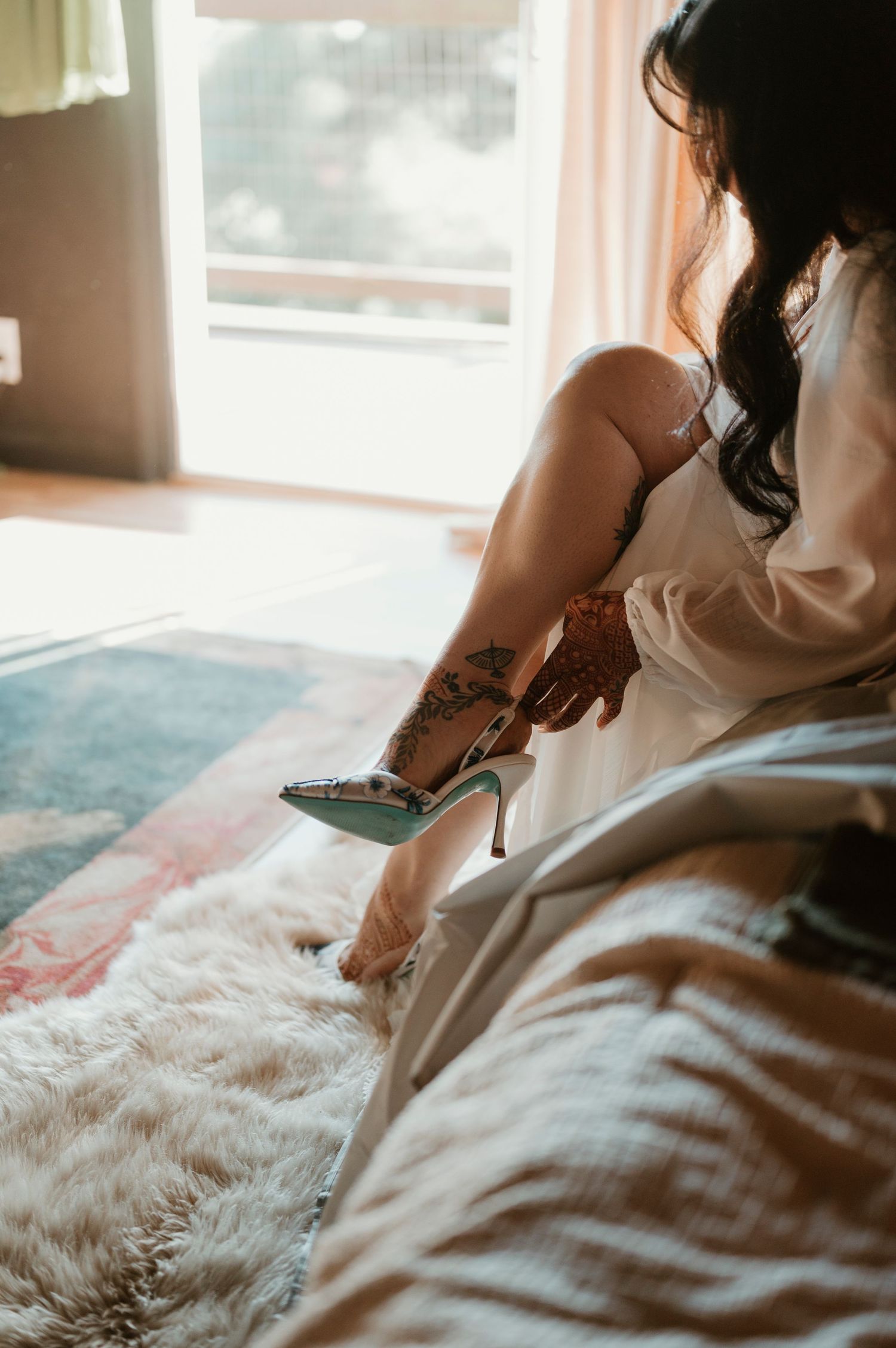 Person in white robe putting on elegant high heel shoes in soft morning light.