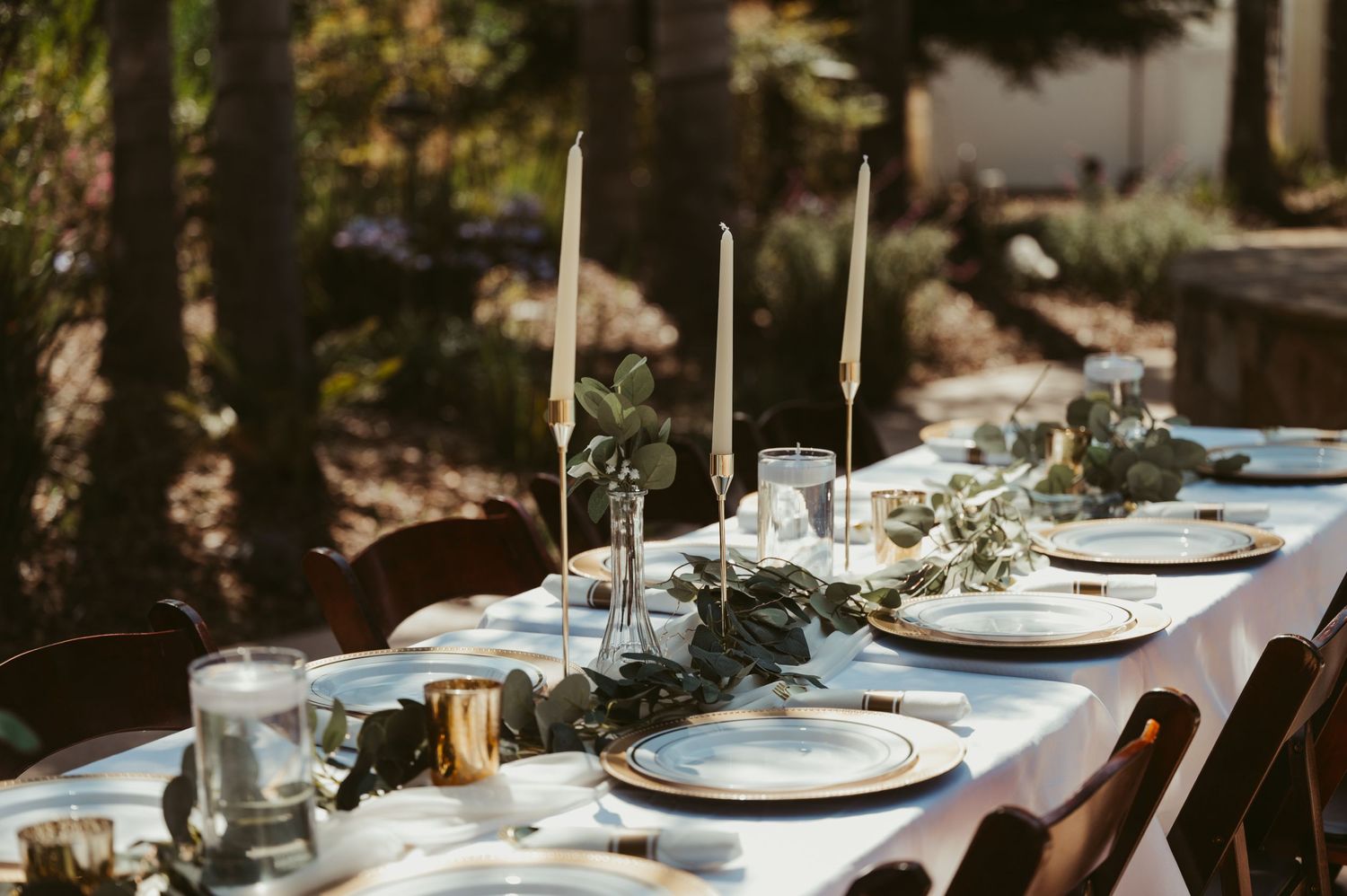 Elegant outdoor table setting with white linens, candles and natural decor.