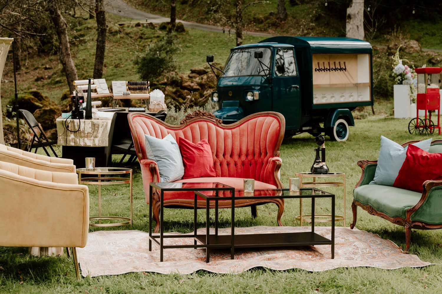 Vintage lounge setup with red velvet settee and green delivery truck in outdoor garden setting.