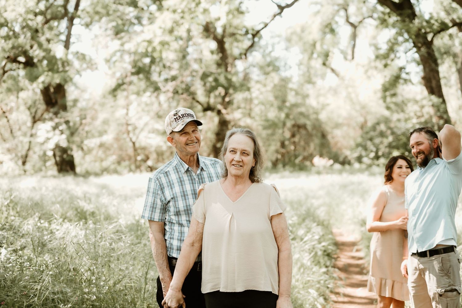 People walking together on a sunlit woodland trail surrounded by trees on a bright summer day.