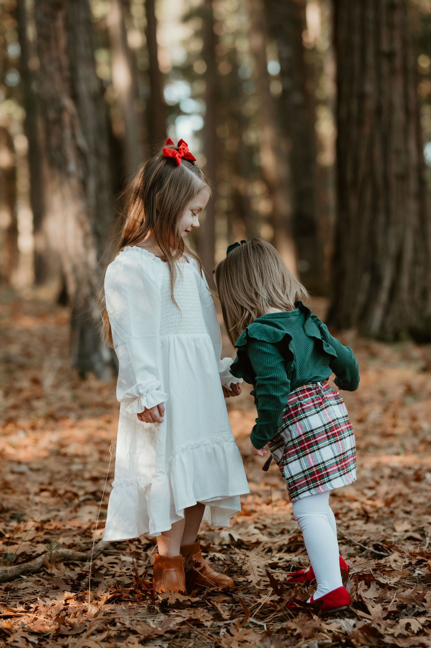 Two children in fall clothing explore a forest floor covered in autumn leaves while playing together.