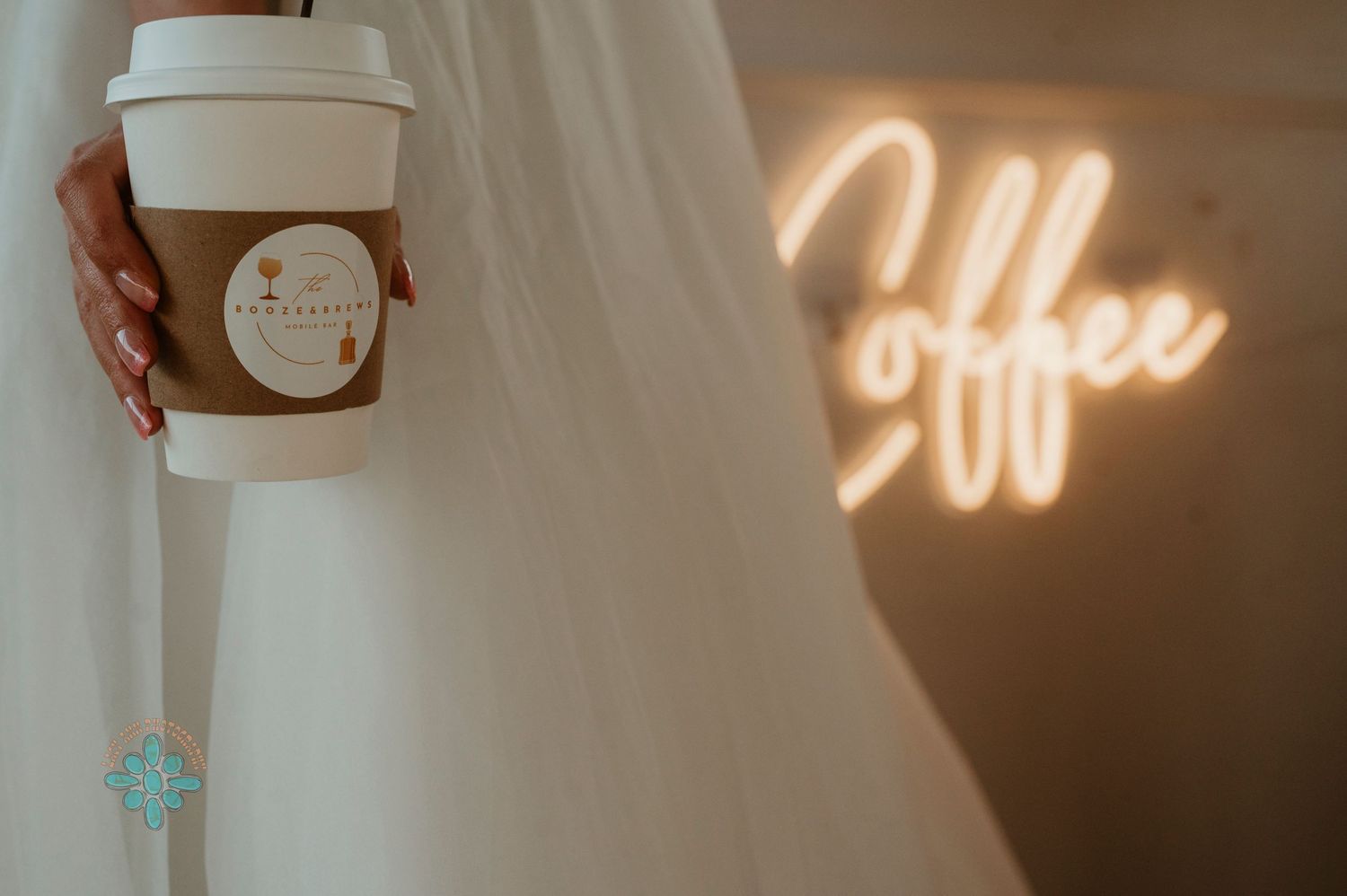 Hand holding coffee cup against white fabric with illuminated coffee sign in background.