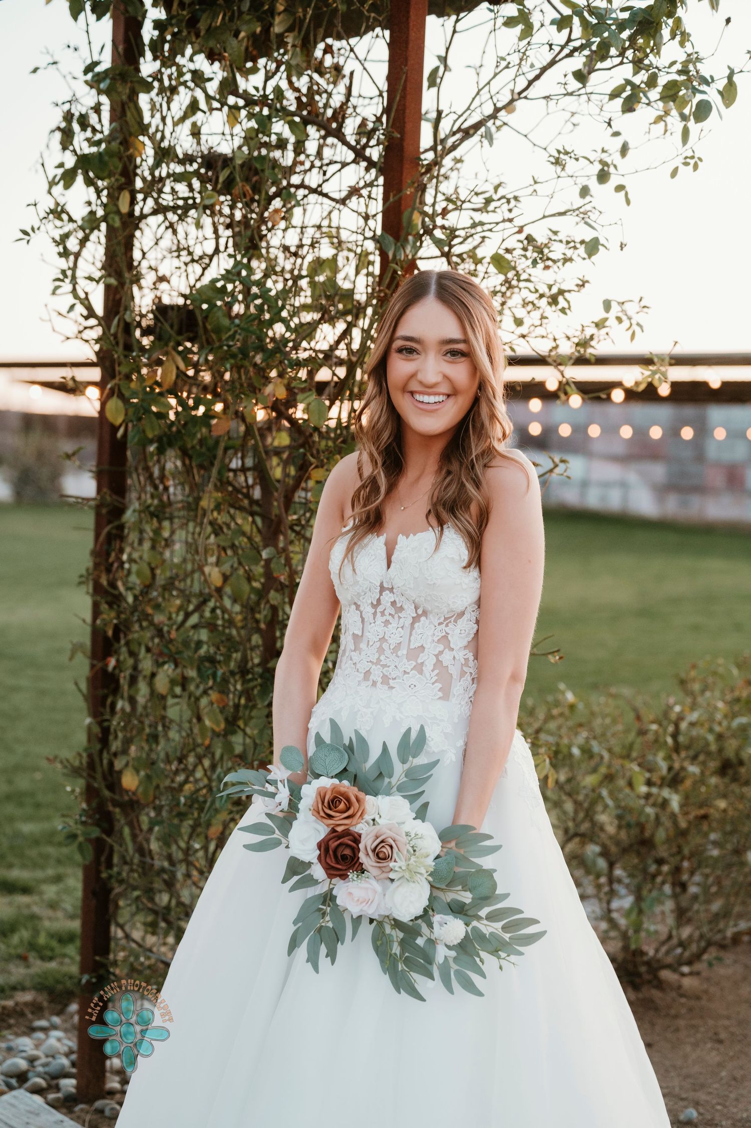 Bride holding floral bouquet with roses and greenery in outdoor garden setting.
