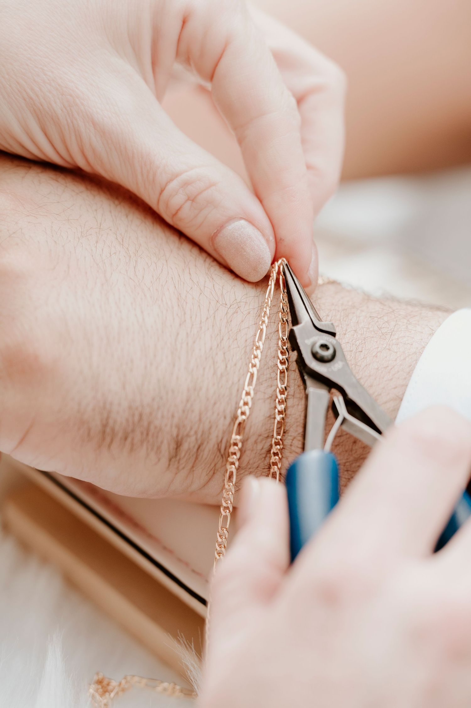 Close-up of hands working with jewelry pliers and delicate gold chain.