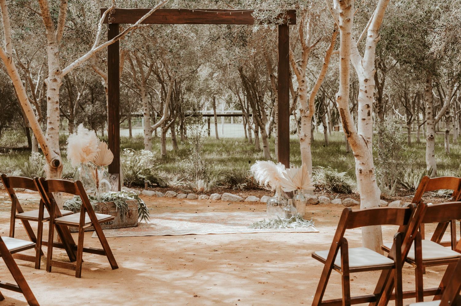 Rustic wooden chairs set up for an outdoor ceremony with white floral decorations in a wooded setting.