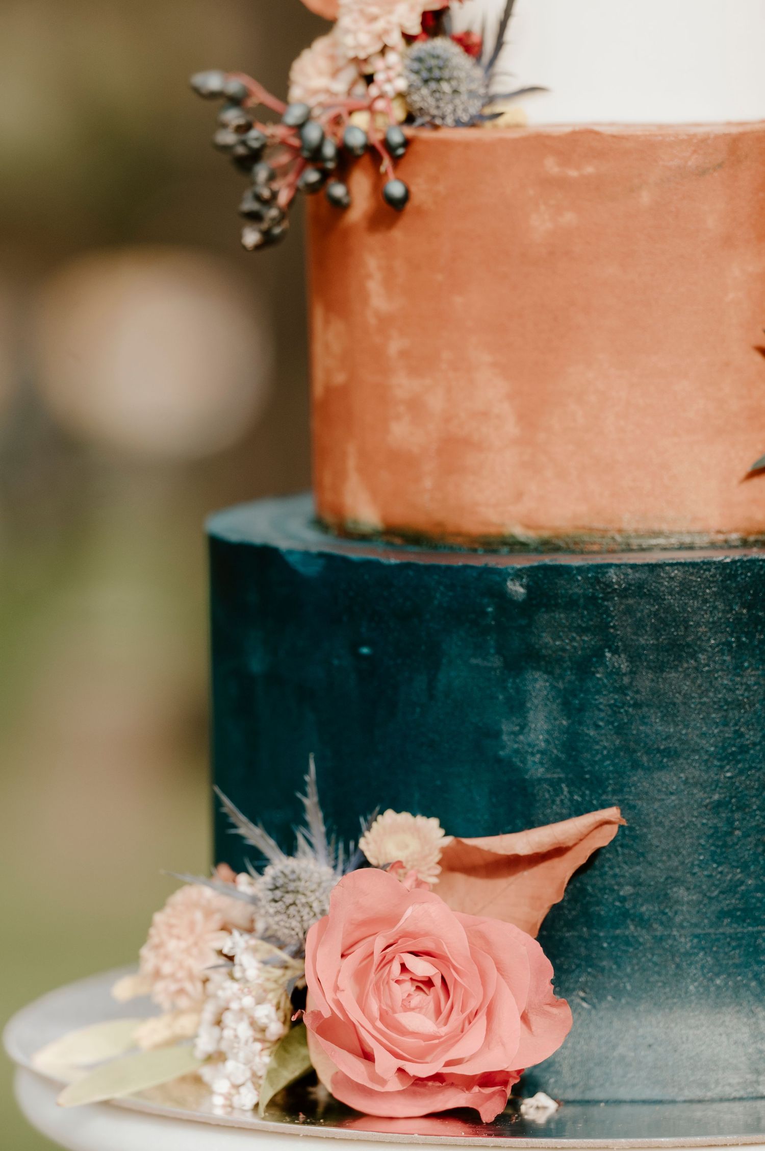 Two-tiered wedding cake with coral pink and navy blue colors decorated with fresh flowers.