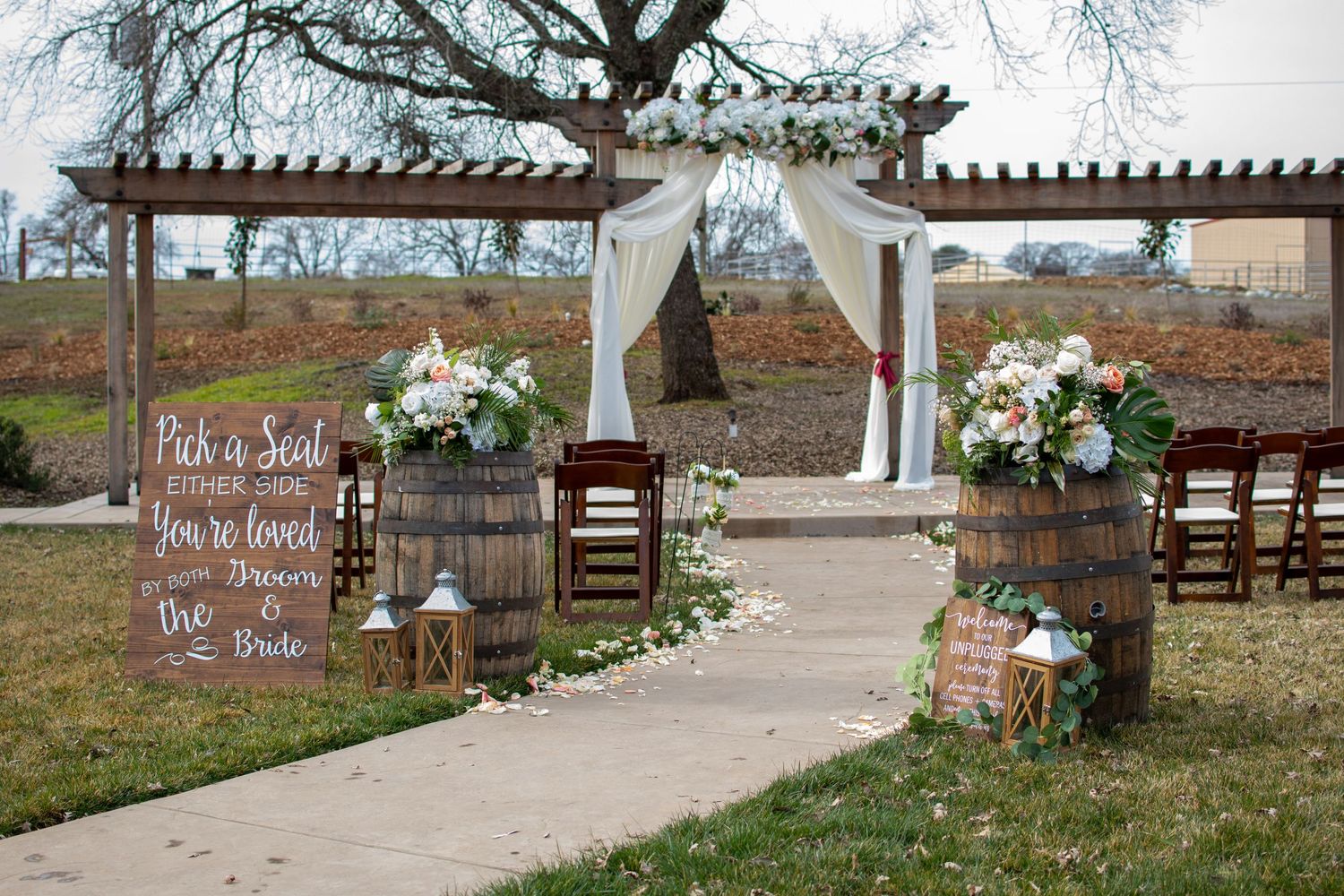 Rustic outdoor wedding ceremony setup with wooden pergola and welcome sign.