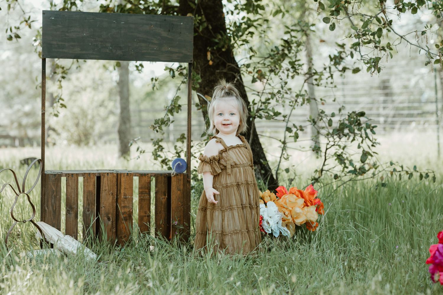 Pink and orange flowers arranged near a rustic wooden fence in a sunny garden setting.