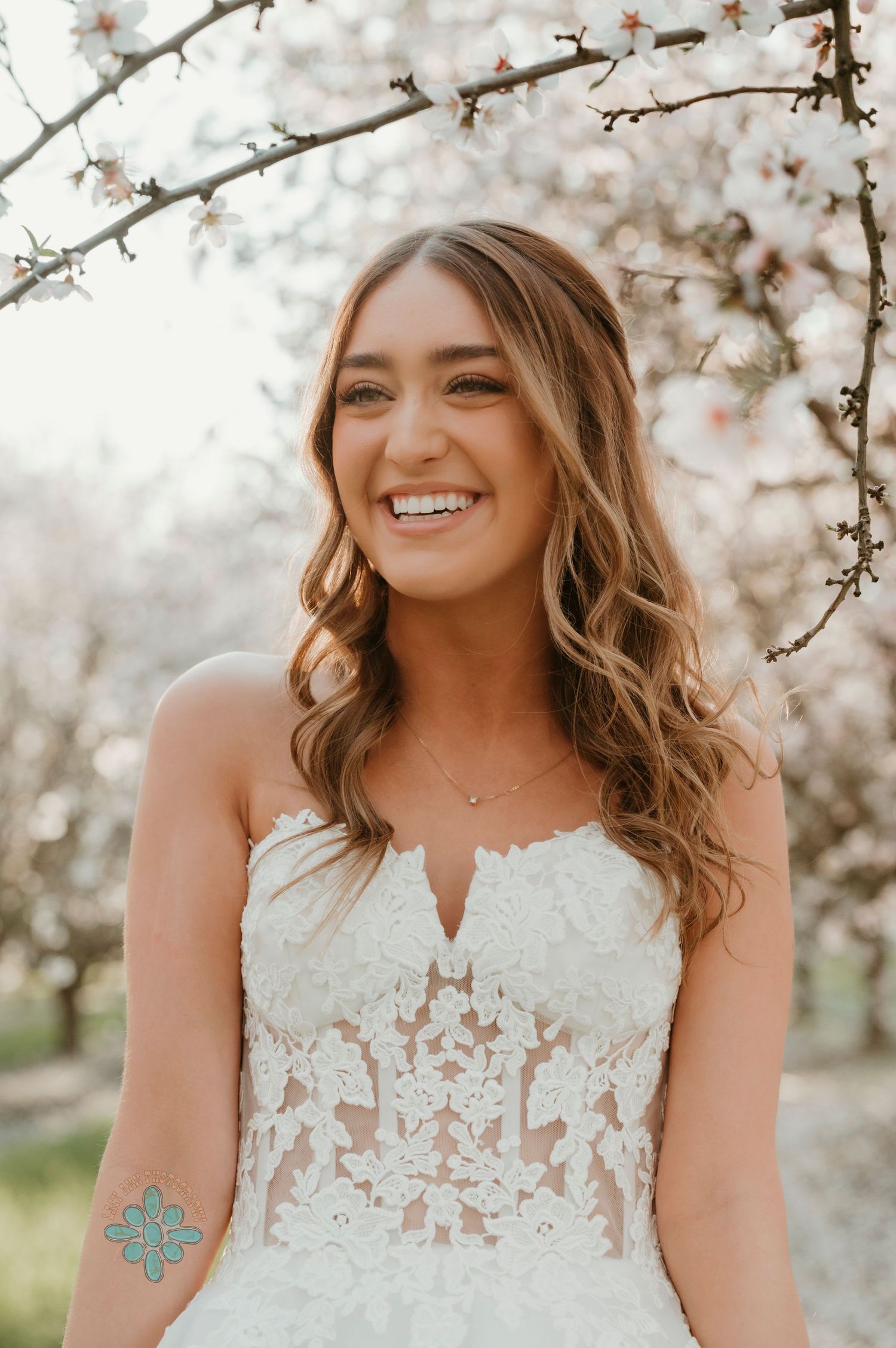 A bride poses under blooming cherry blossoms wearing a detailed lace bodice wedding gown.
