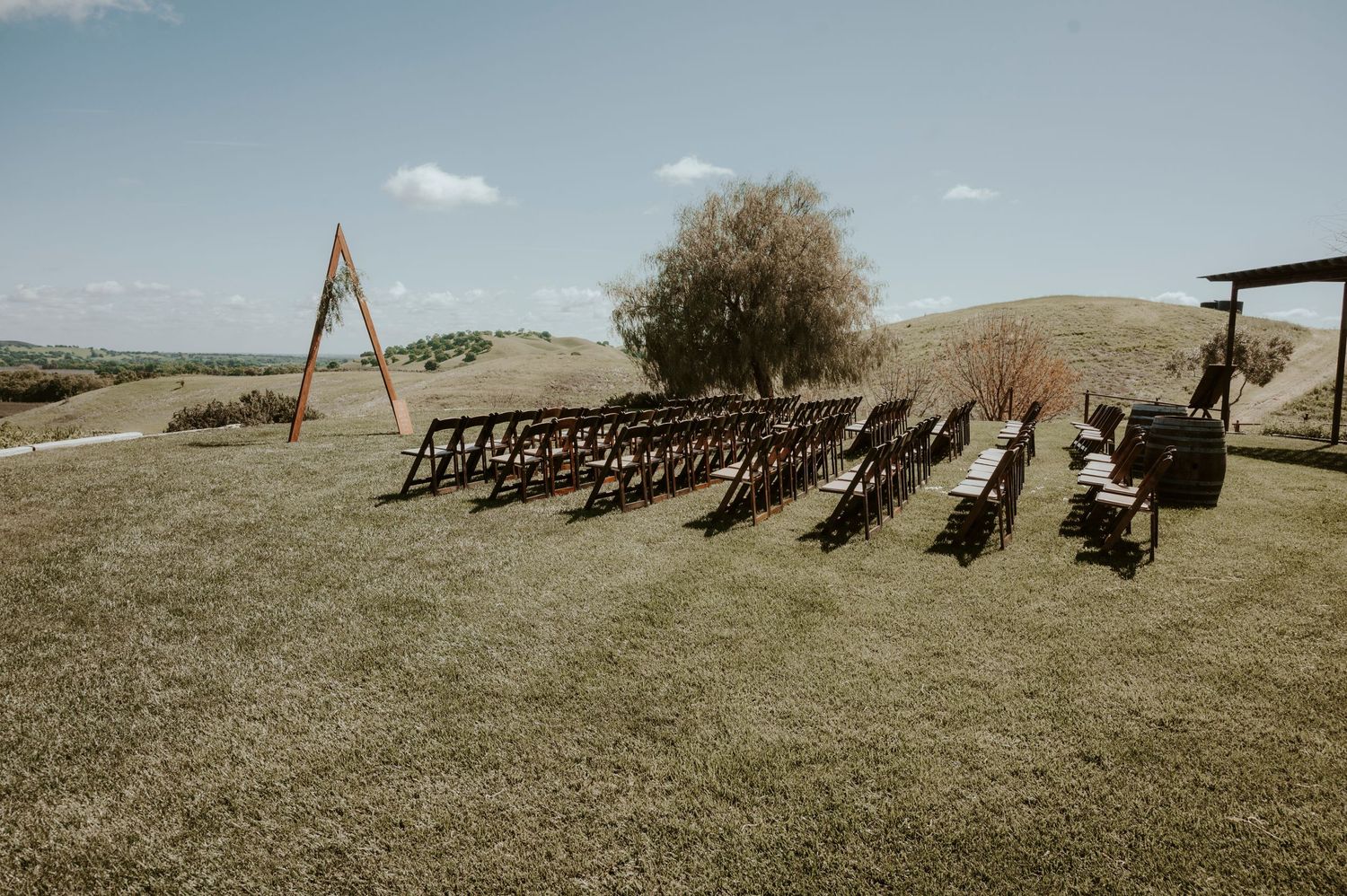 Rows of dark wooden chairs set up for an outdoor ceremony with mountain views and triangular arch.