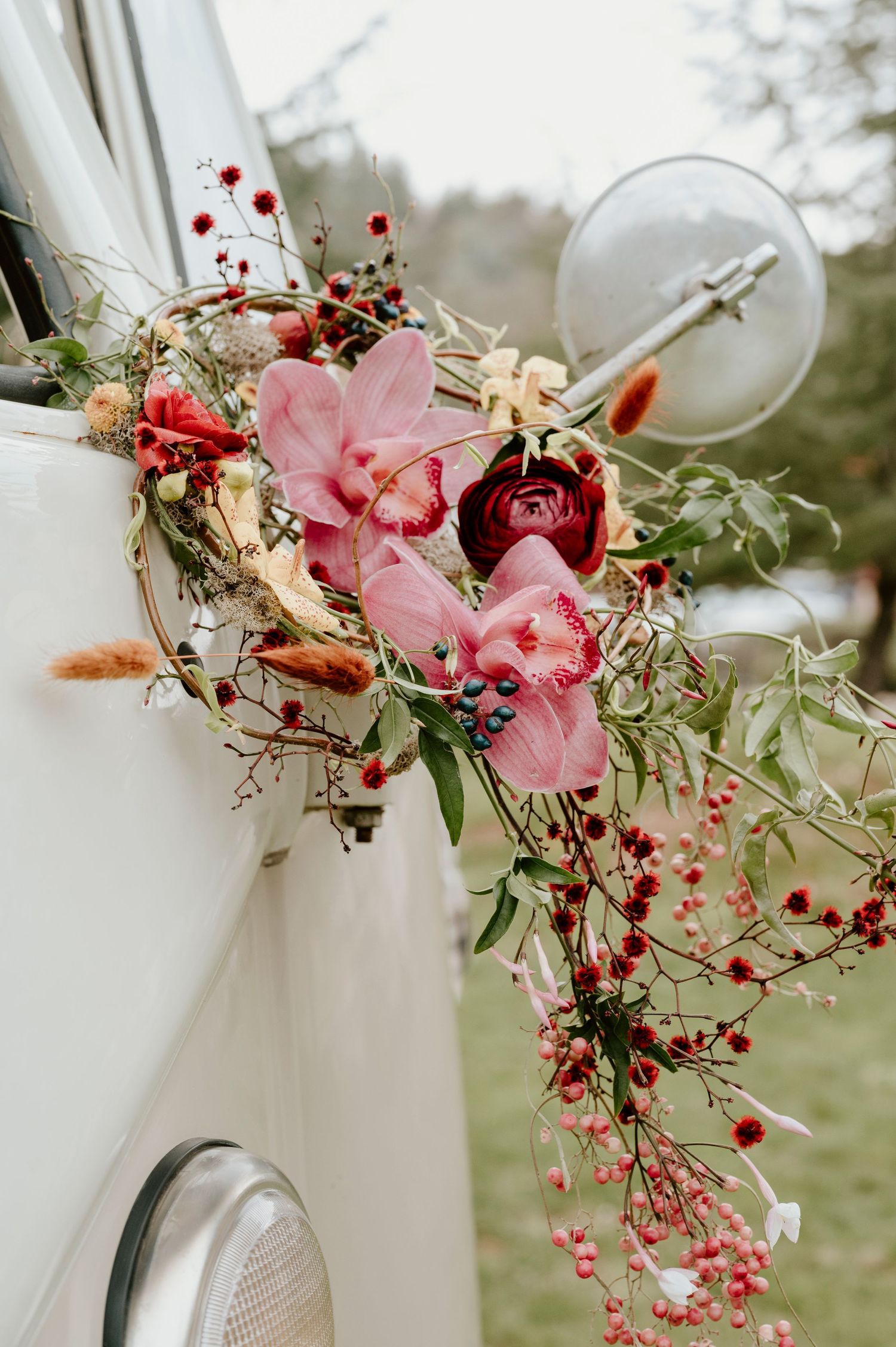 Pink orchids and red berries adorning a classic car's side mirror decoration.