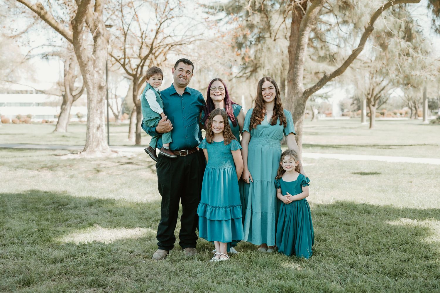 Family wearing coordinated teal and black outfits poses together outdoors in a natural setting.