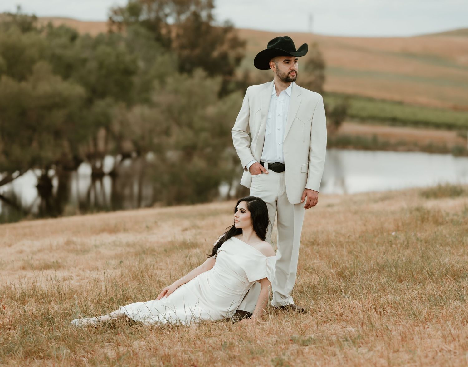 Romantic countryside photoshoot with couple in white attire against rolling hills.