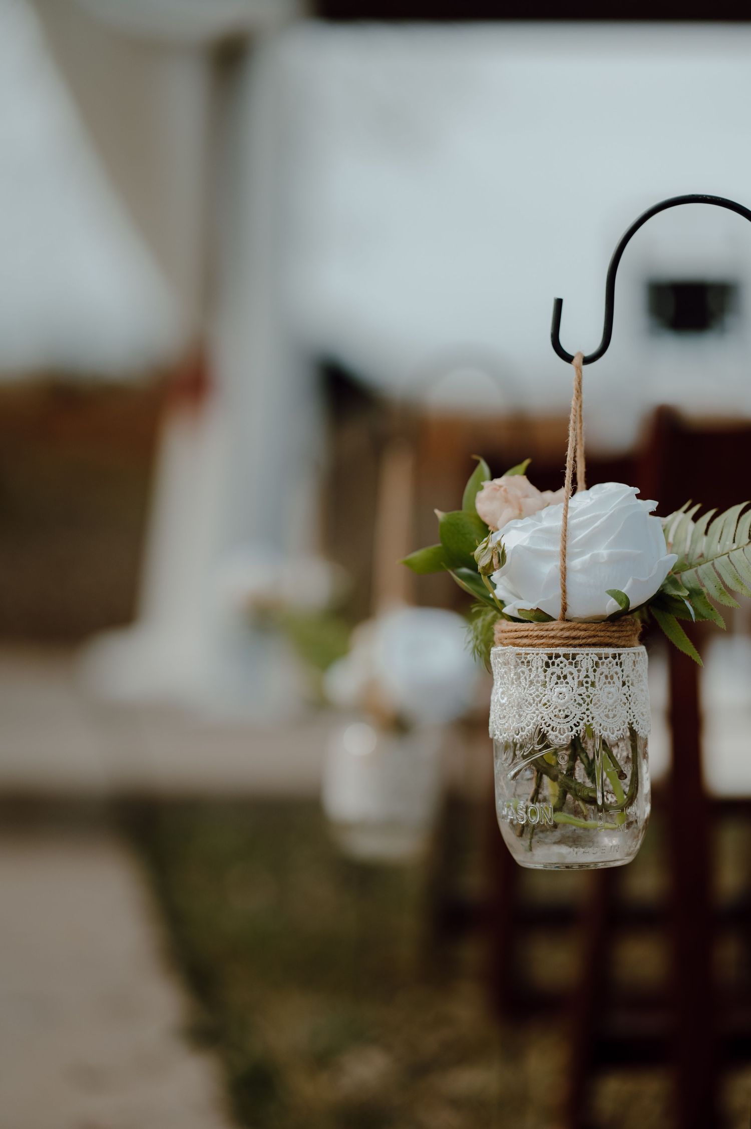 Mason jar with lace decoration and white flower hanging as rustic wedding aisle decor.