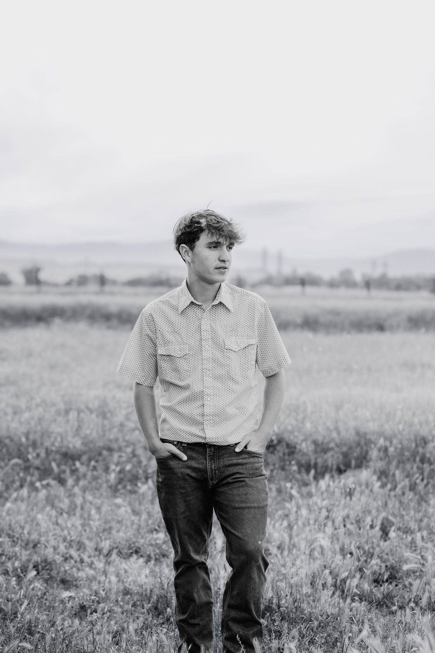 Young man in button-up shirt standing in open field, black and white photo.