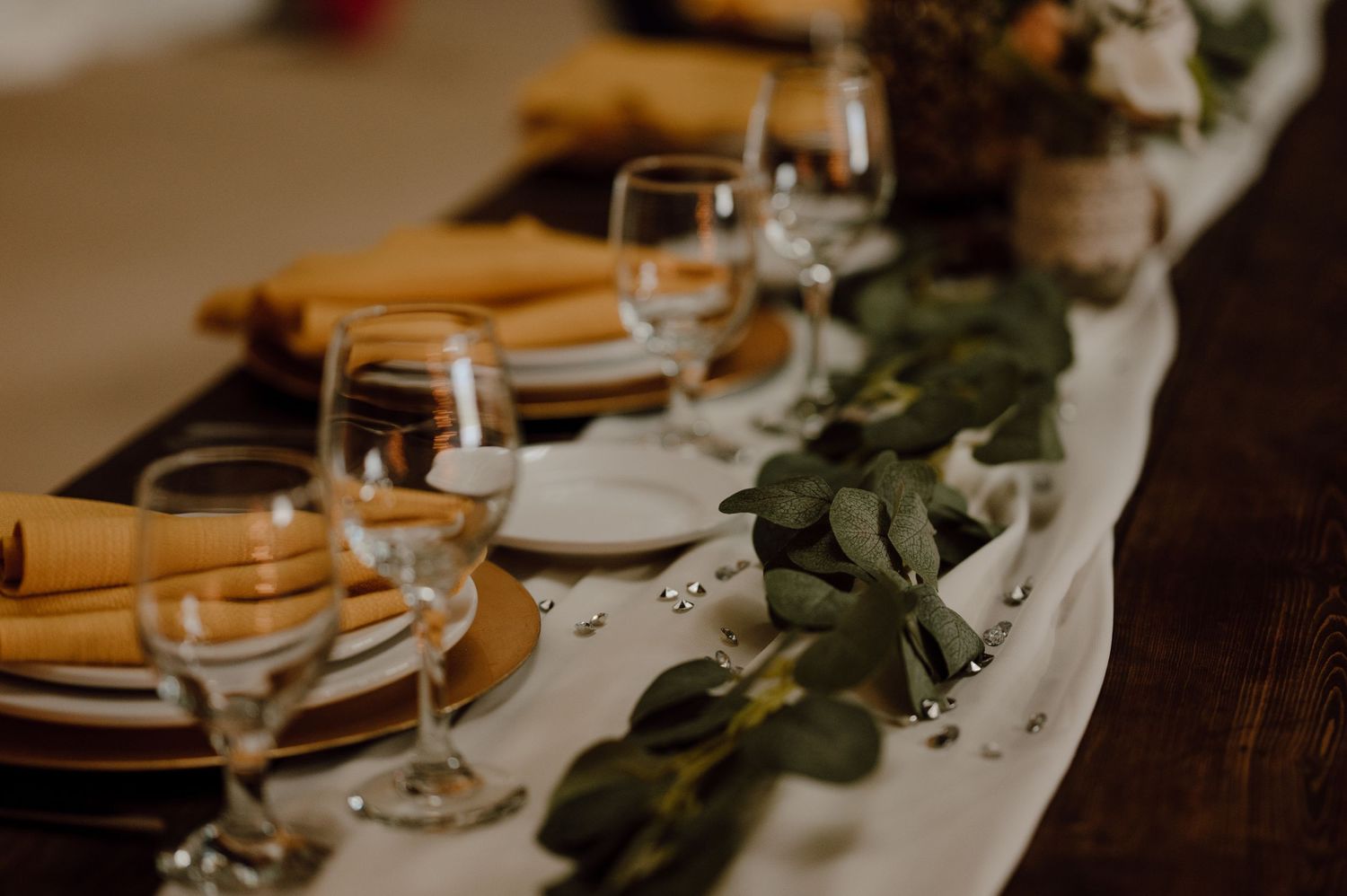 Wedding reception table setting with yellow napkins and eucalyptus garland runner.