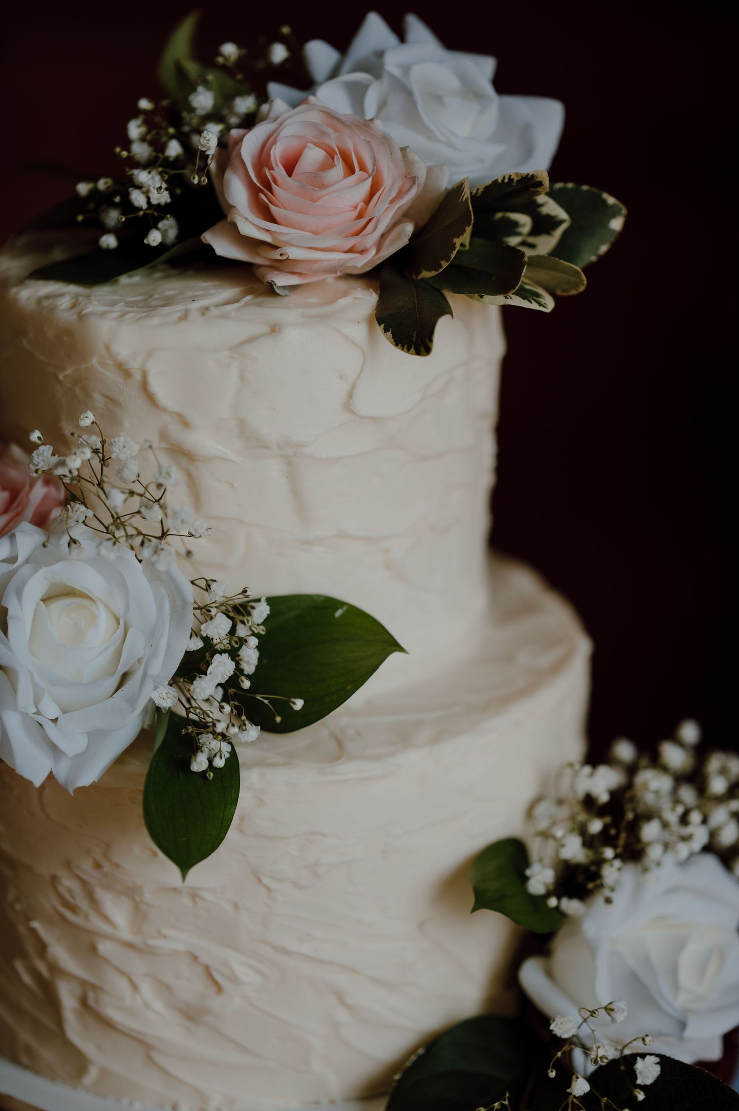 Elegant white wedding cake decorated with pink and white roses, baby's breath, and green foliage.