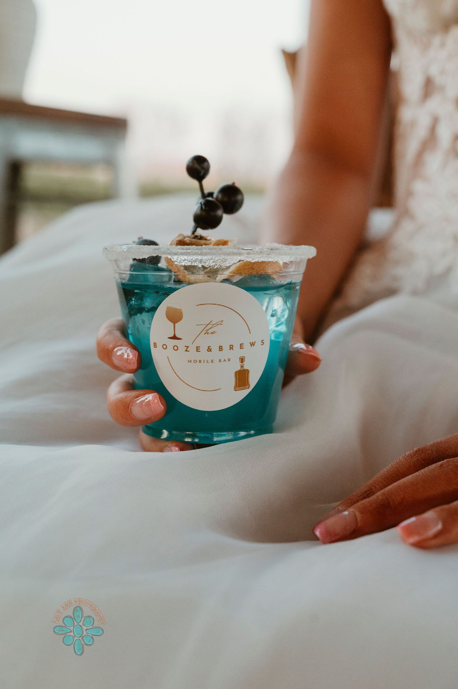 Close-up of hands holding a bright blue decorated cocktail on white fabric.