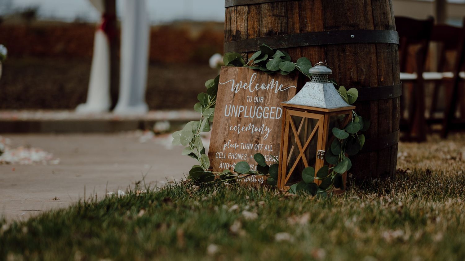 Wooden wedding sign with lantern and greenery displayed on rustic barrel.