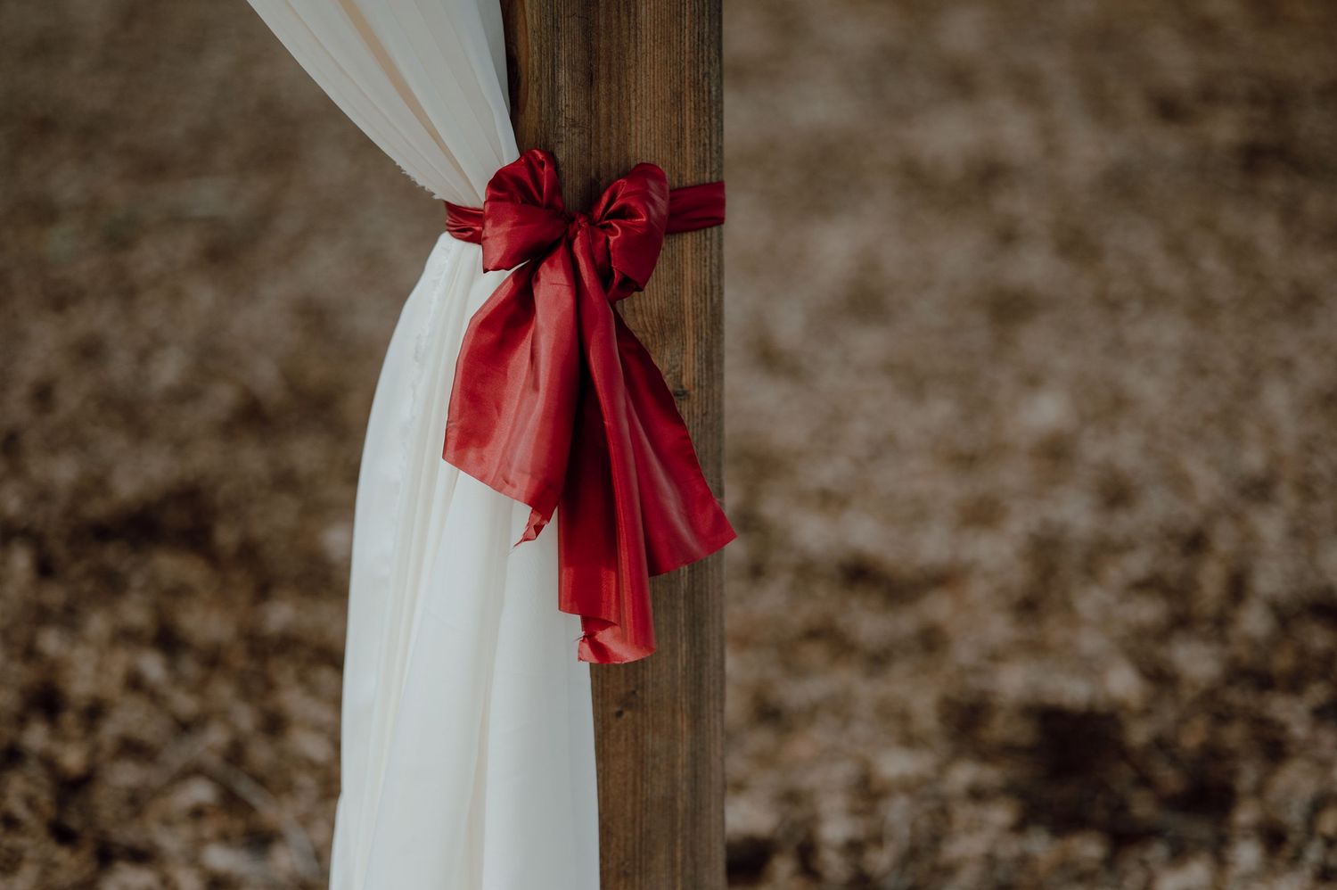 White fabric tied with a red satin bow on wooden post for wedding ceremony.