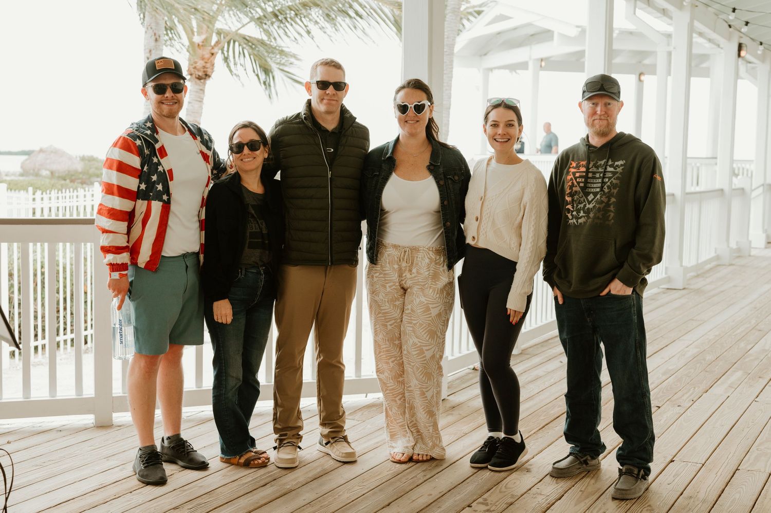 Group of people posing on wooden deck with palm trees in background.
