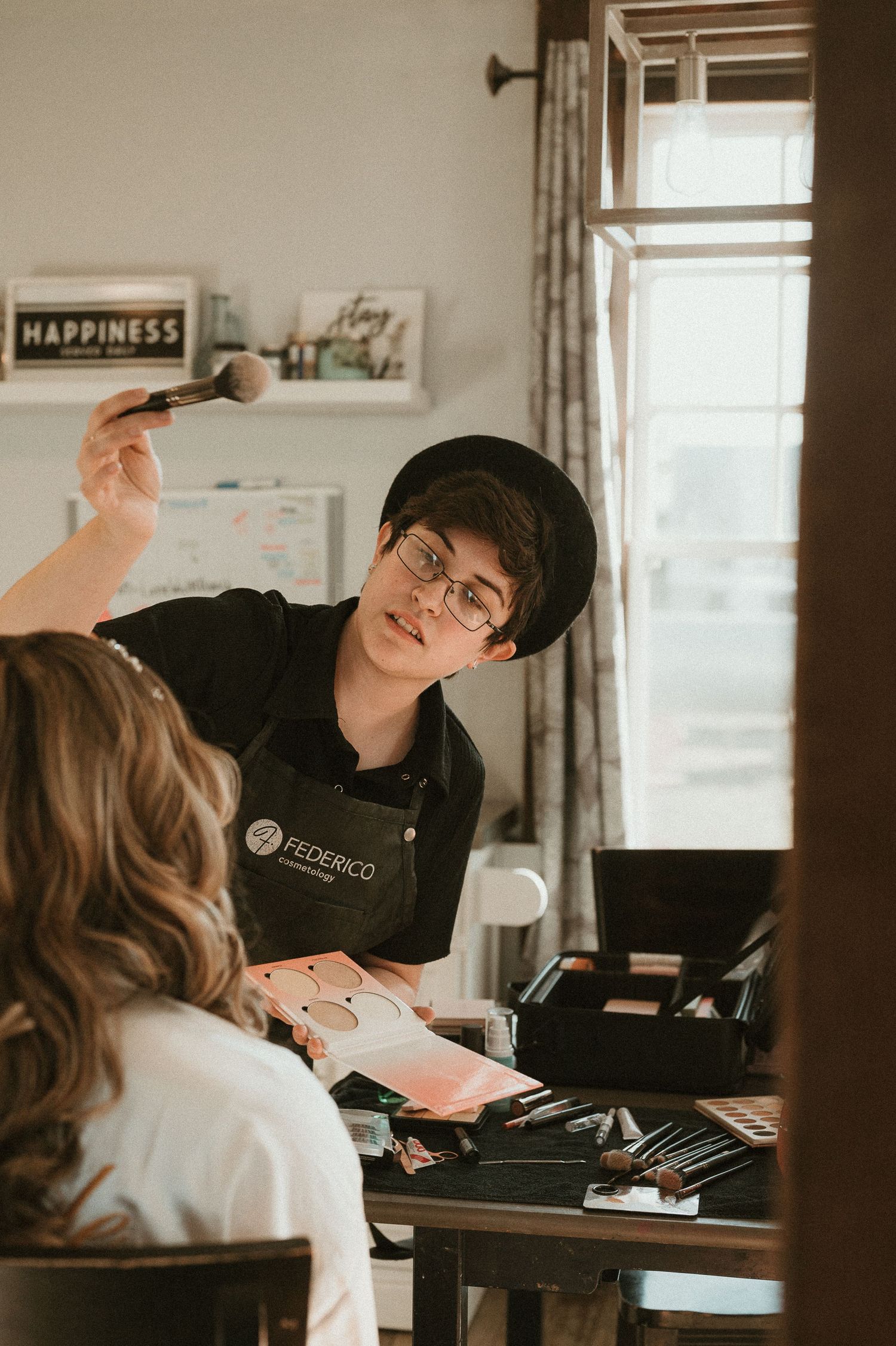 Professional makeup artist working with client in natural window light.