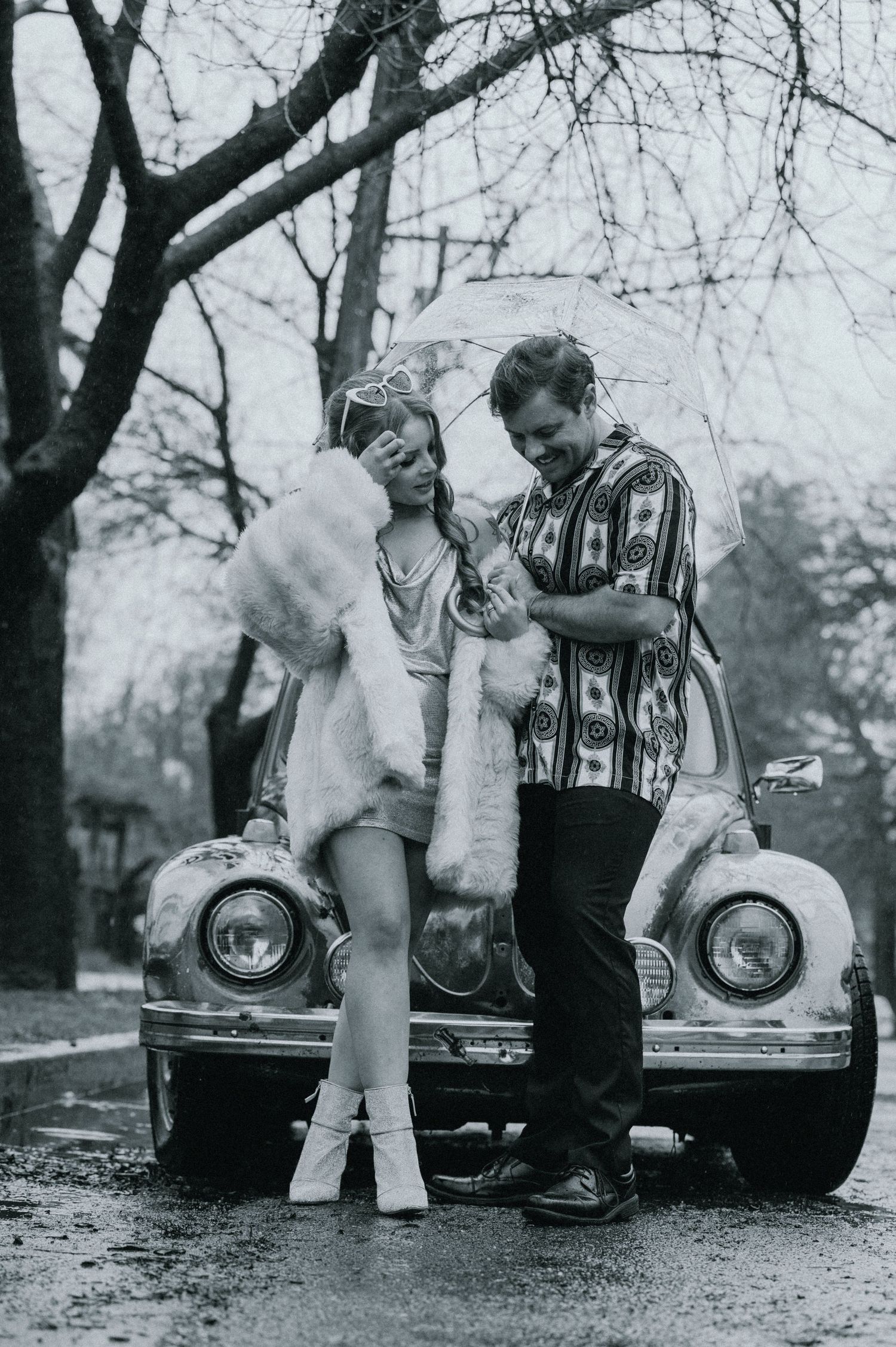 A black and white photo series showing people interacting near a vintage car under bare winter trees.