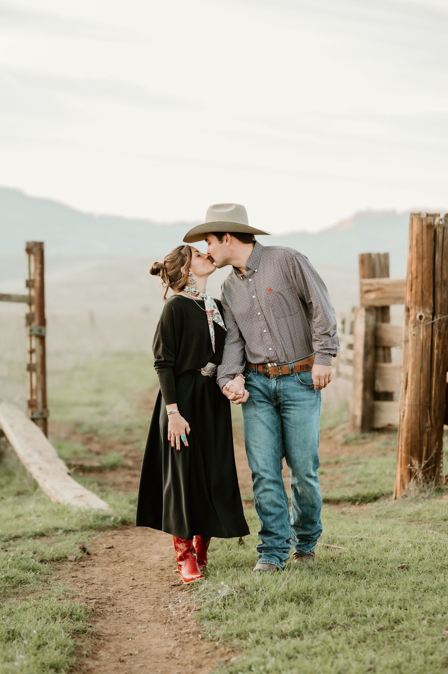A romantic couple shares a tender moment on a rustic ranch with mountains in the background.