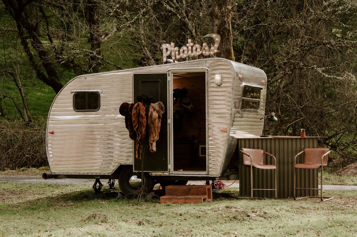 Vintage white camper trailer converted into photo booth with retro chairs outside.