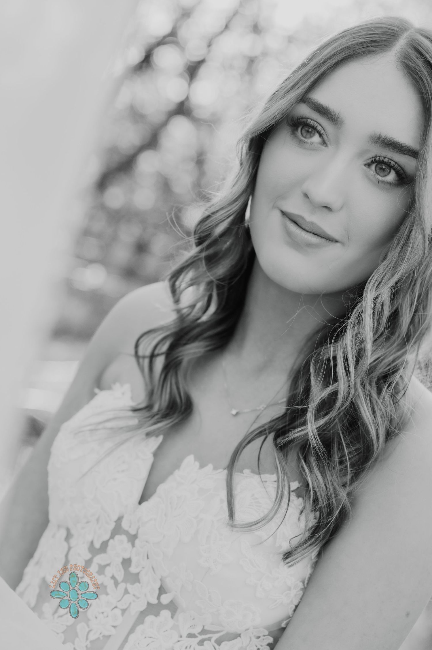 A black and white portrait shows a woman in a lace wedding dress with soft bokeh background.