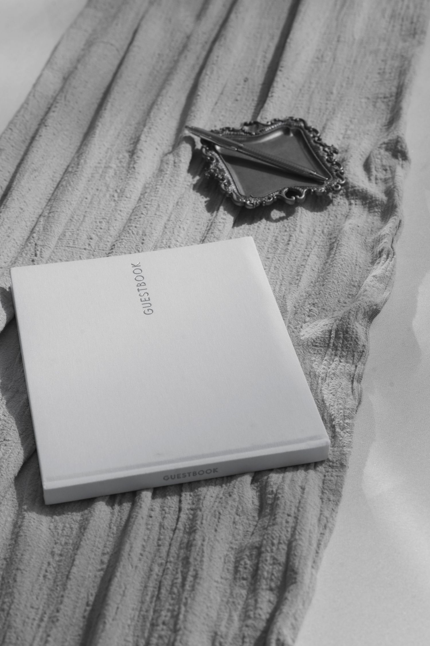 Black and white photo of jewelry box and notebook on textured fabric.