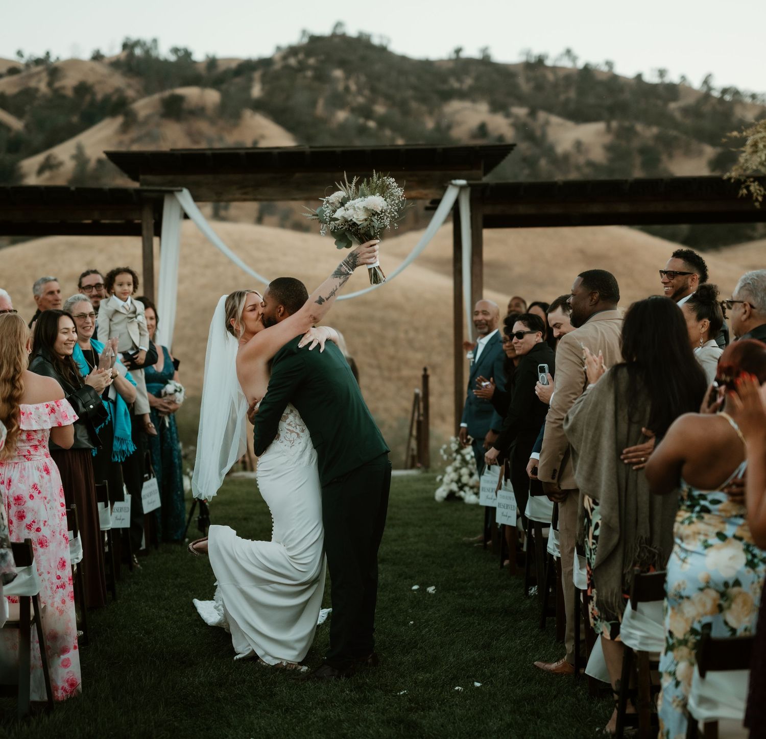 Wedding ceremony and guests gathered on a grassy field at sunset.