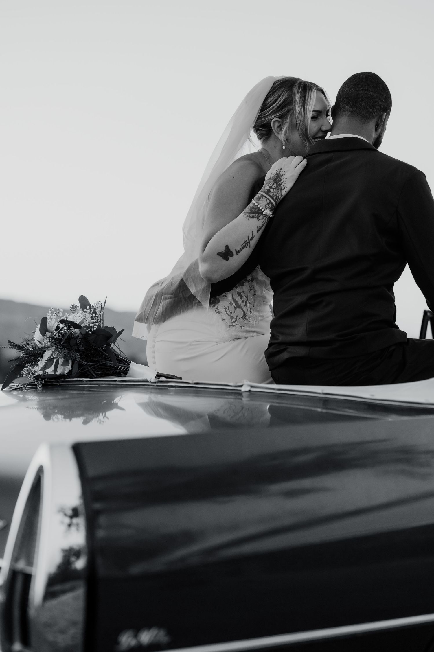 Black and white photo of newlyweds sitting in classic car.