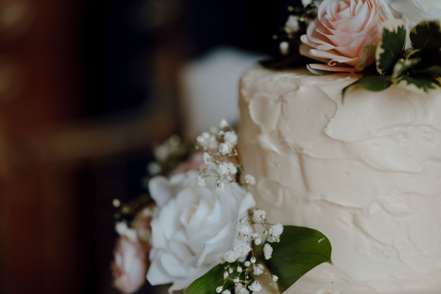Close-up of white wedding cake detail with roses and baby's breath floral decorations.