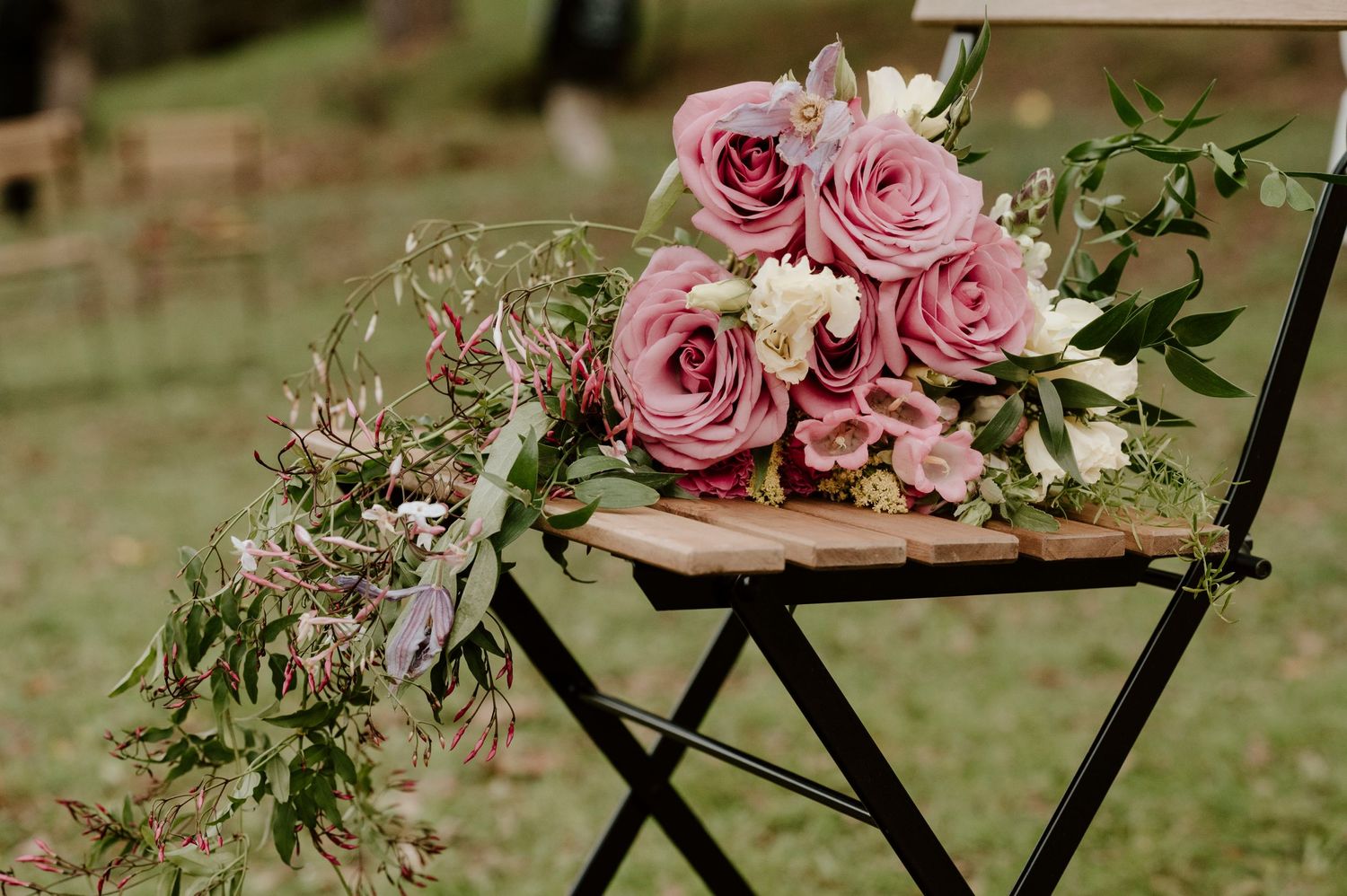 Pink roses and greenery arrangement on rustic wooden folding chair outdoors.