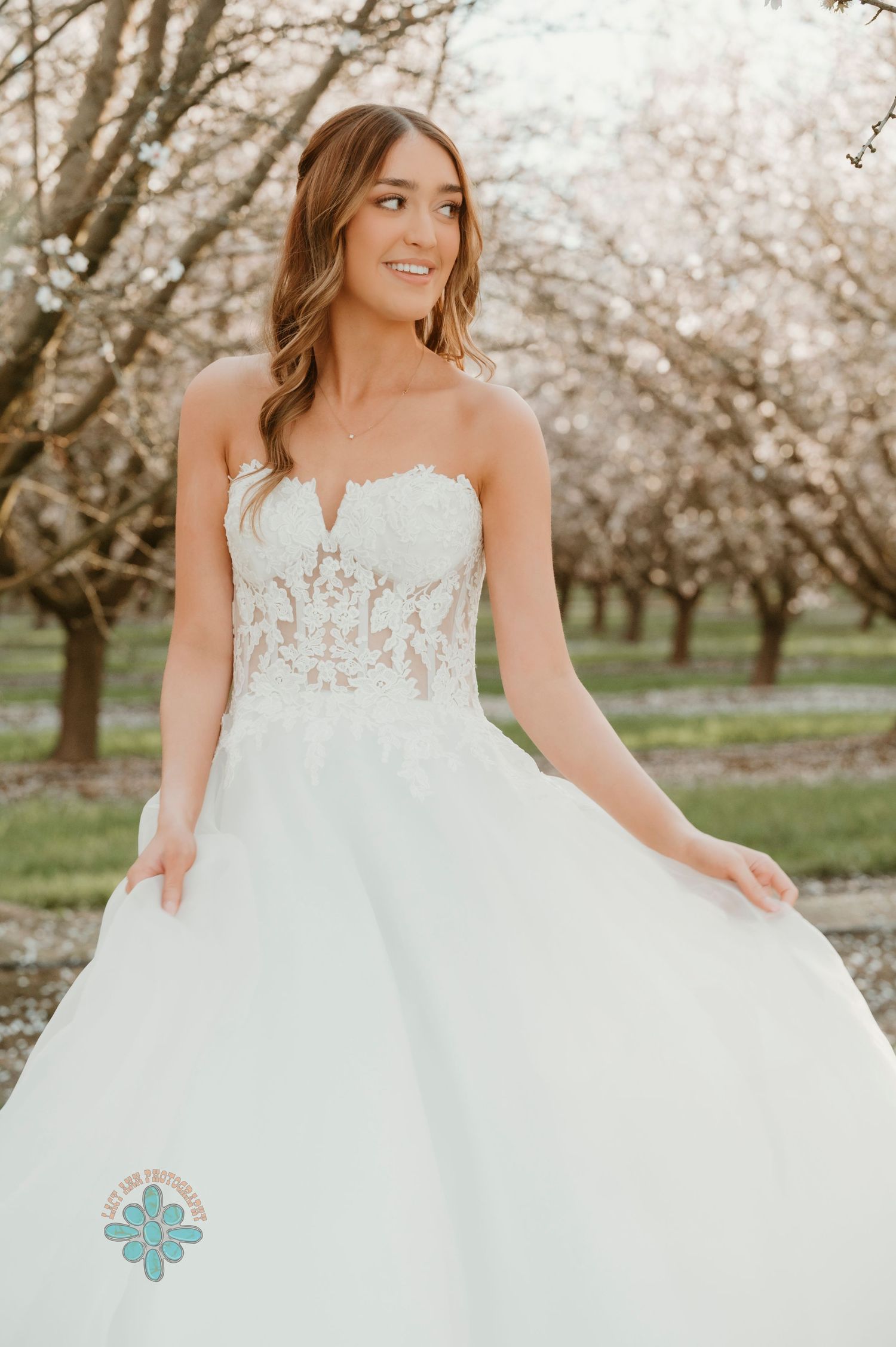A bride wearing a strapless ballgown twirls in an orchard of spring blossoms.