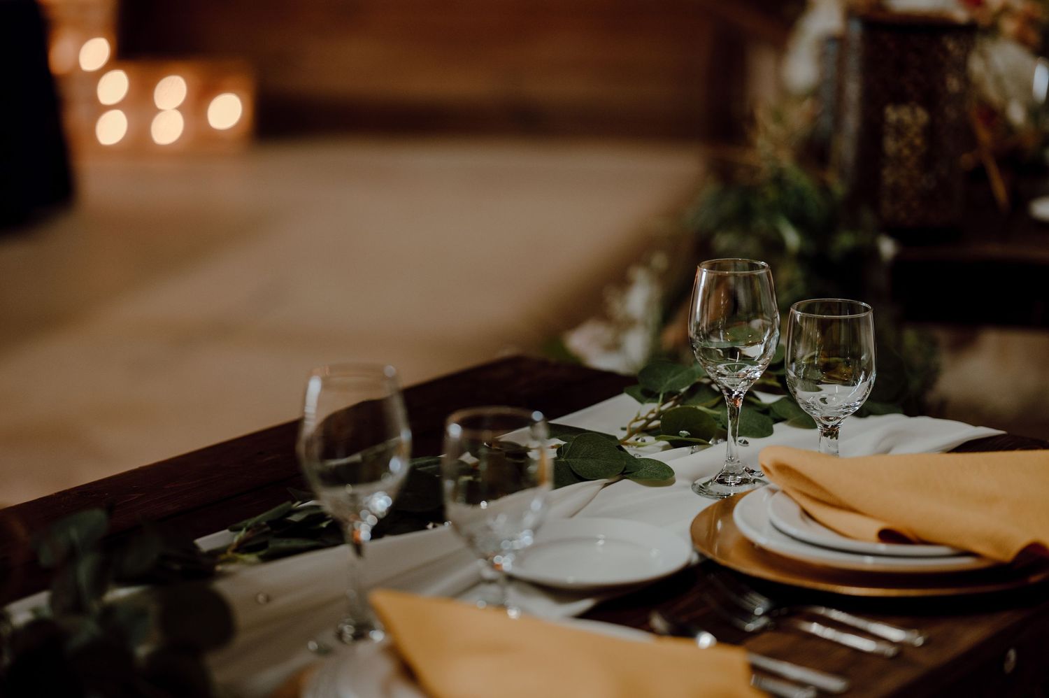 Elegant table setting with wine glasses, white plates, and yellow napkins at a wedding reception.