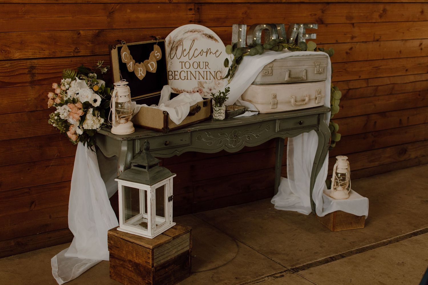 Rustic welcome display with vintage decor and white fabric on wooden table.