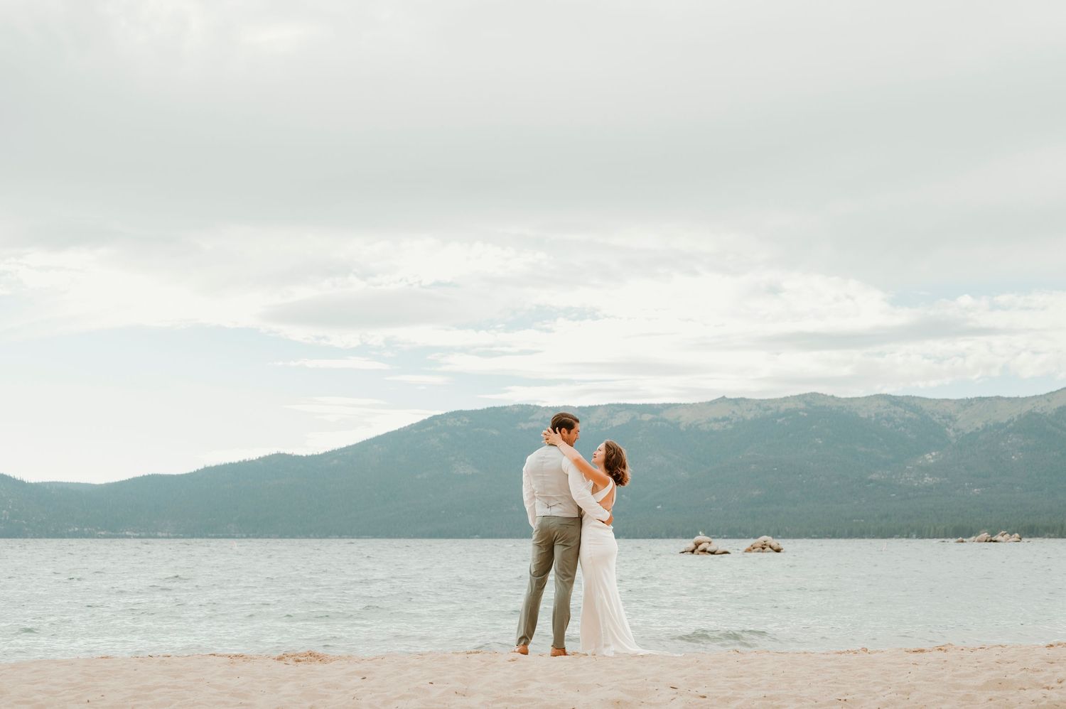 Newlyweds share an intimate moment against a scenic mountain lake backdrop.
