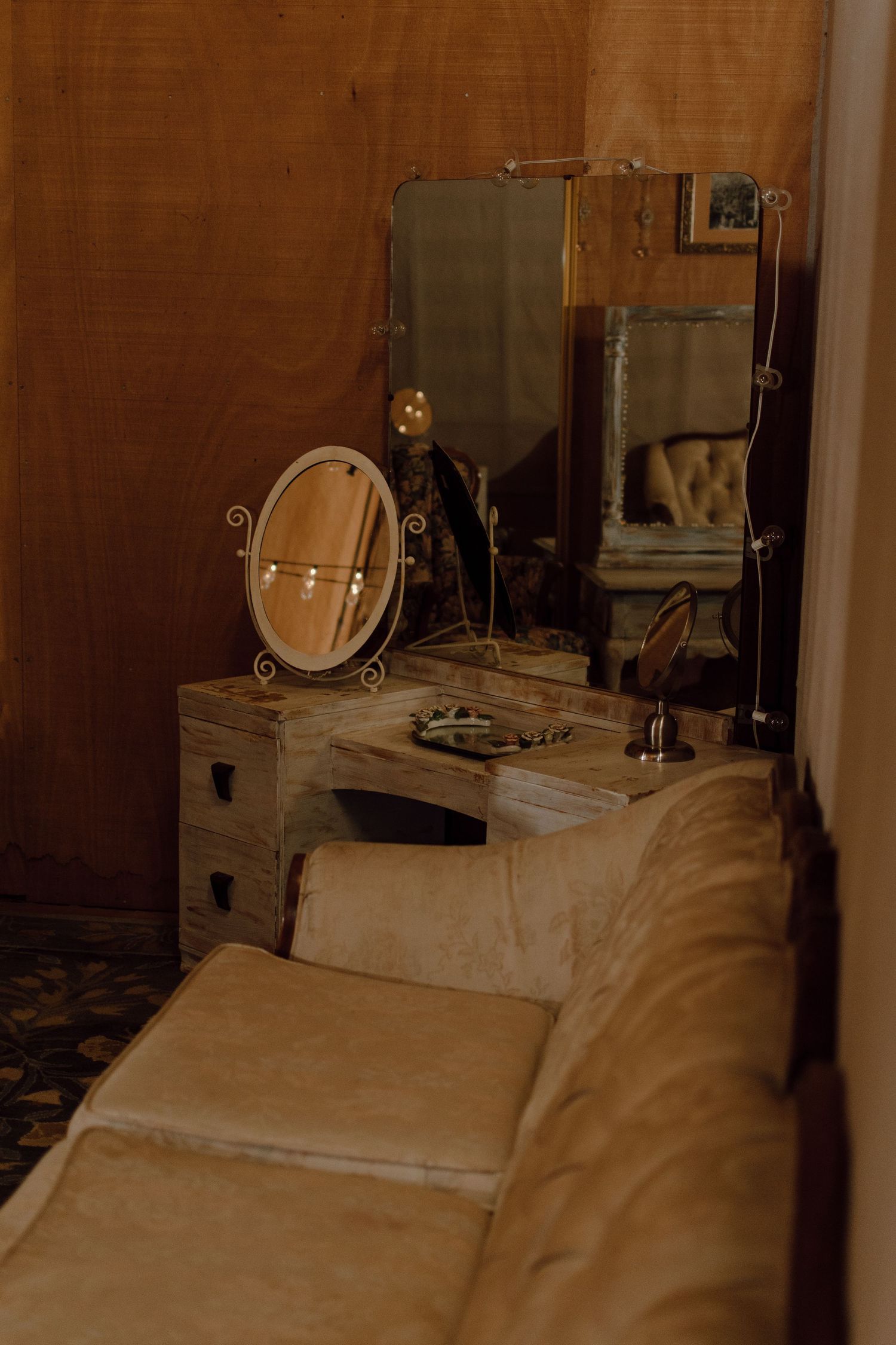 Antique vanity setup with mirrors and cushioned bench in a moody, dimly lit room.