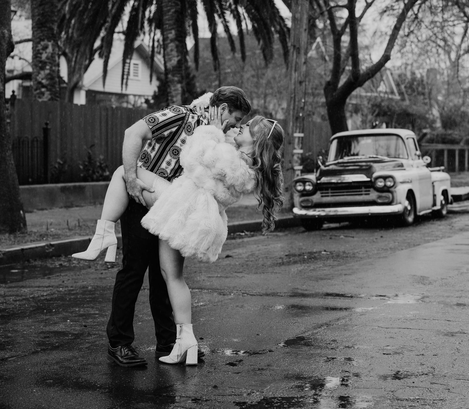 A black and white photo sequence showing a couple dancing in the rain on a city street with vintage cars visible.