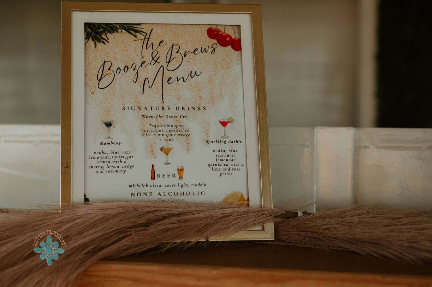 A framed bar menu displaying signature cocktail options at a wedding reception.
