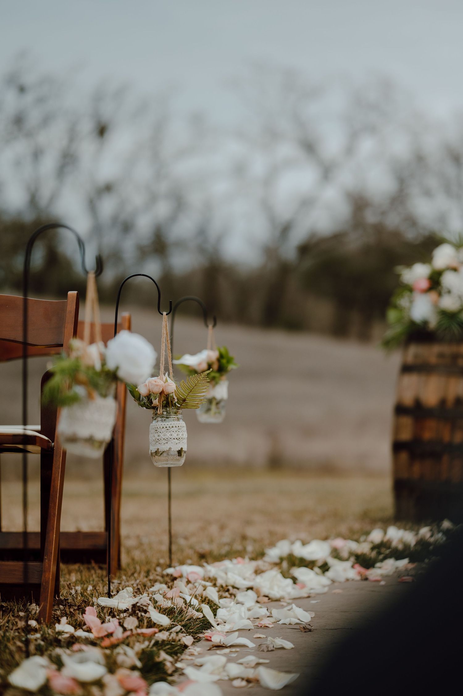 Mason jar lanterns with flowers line a wedding ceremony aisle path.