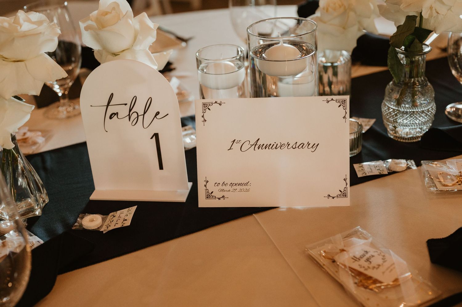 Elegant wedding reception table setting with calligraphy table number and place cards in warm lighting.
