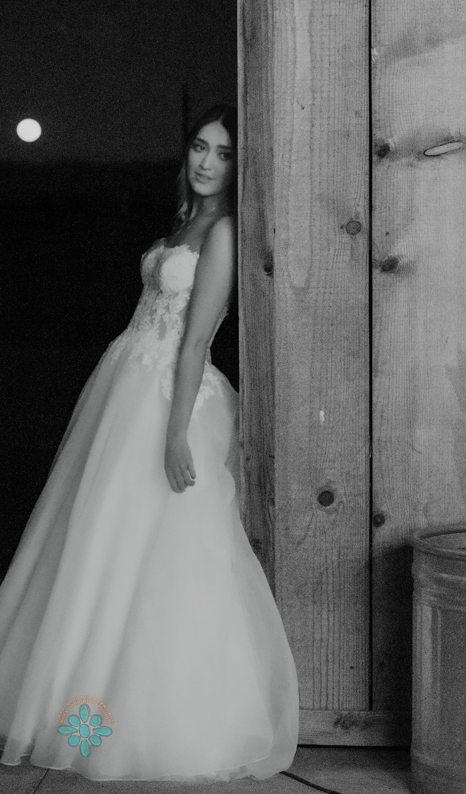 A bridal portrait in black and white showing an elegant wedding gown against a rustic wooden background.