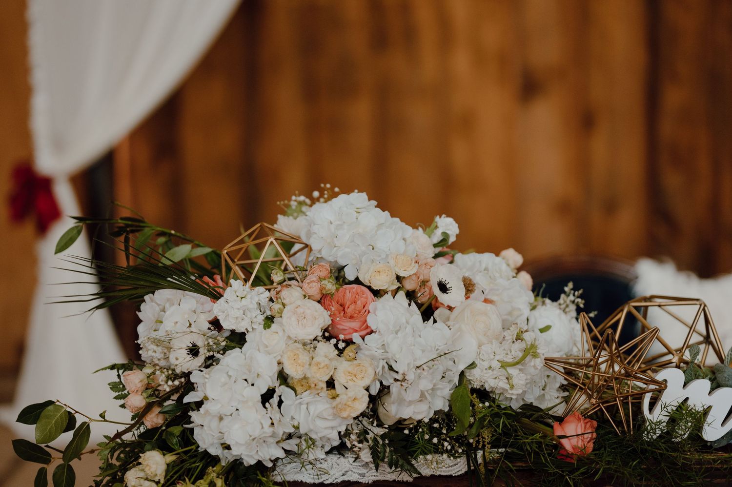 Luxurious white and pink floral arrangement with geometric accents against wooden backdrop.