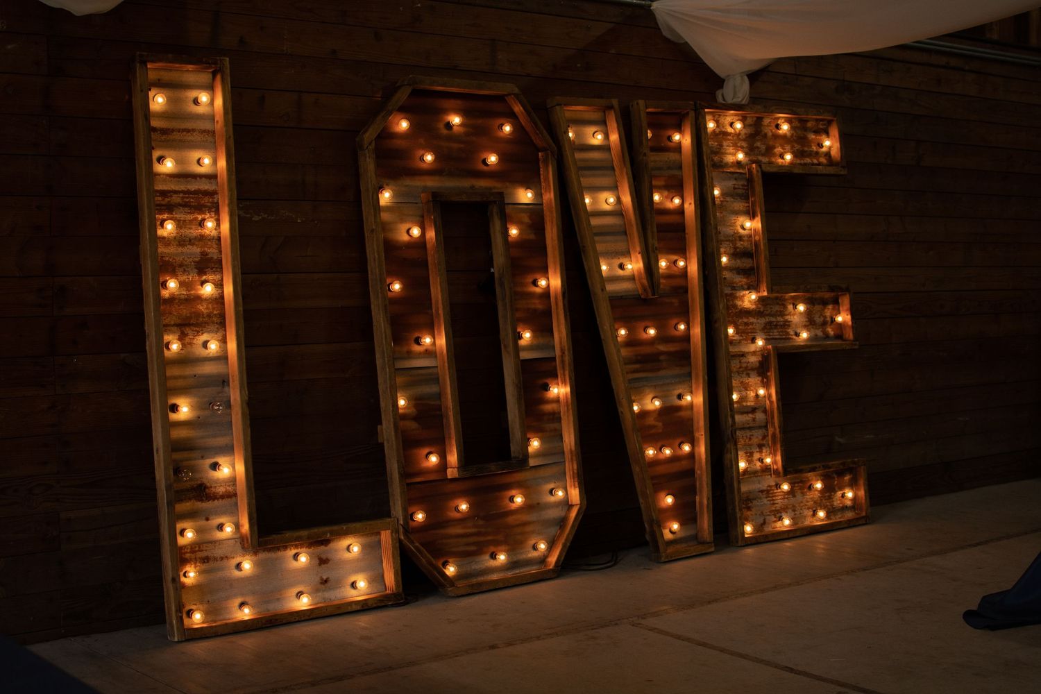 Large illuminated LOVE marquee letters create romantic wedding decor against brick wall.