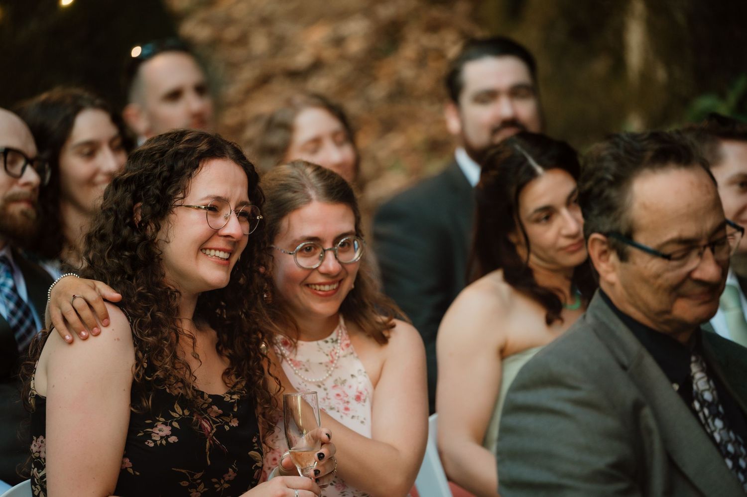 Wedding guests share joyful laughter during an outdoor ceremony with warm lighting and natural scenery.